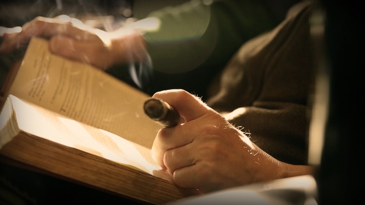 Man reading book alone while smoking a cigar in the Introvert's Guide to the Cigar Social Life