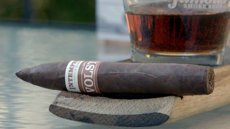 cigar advisor my weekend cigar review roma craft intemperance volstead 1920 - setup shot of the cigar on a whisky barrel stave with glass of spirits in the background