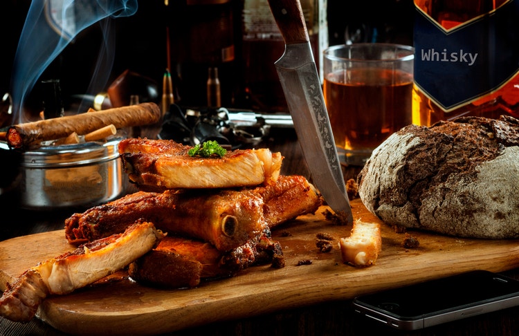 cigar advisor food for thought: using food to choose the best cigar for you - setup shot of meat on a cutting board with whisky and burning cigar in the background
