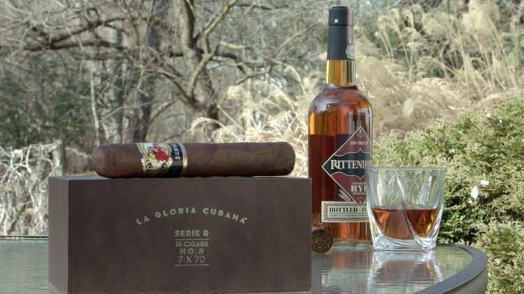 cigar advisor #nowsmoking cigar review of la gloria cubana serie r no. 8 (7" x 70) - setup shot of cigar on box with bottle of spirits and whiskey glass along side