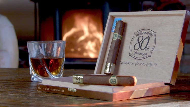 cigar advisor panel review video dunbarton tobacco & trust famous 80th anniversary - setup shot of cigar with whisky and a fireplace in the background