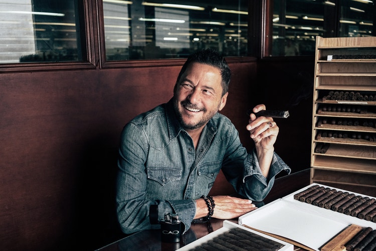 cigar advisor news - cao cigars rick rodriguez retires - portrait of rick sitting at a rolling table and smoking a cigar