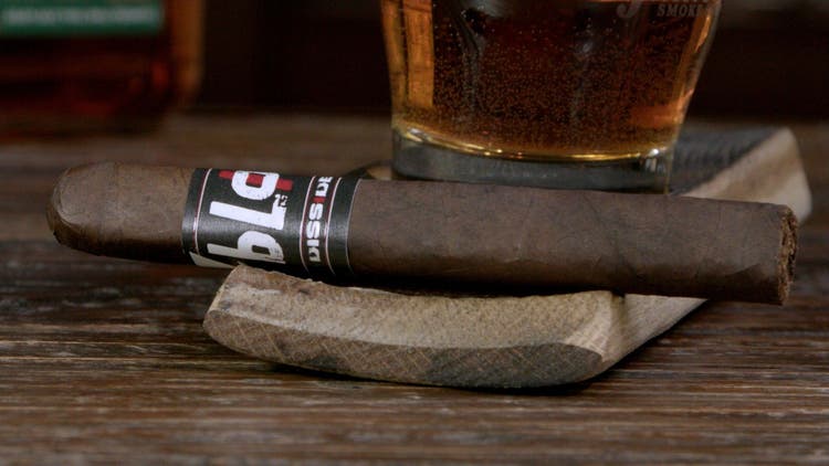 cigar advisor #nowsmoking cigar review dissident bloc - setup shot of cigar on wooden barrel stave with drink in the background