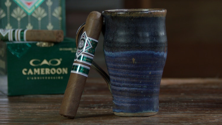 cigar advisor #nowsmoking cigar review of cao cameroon l'anniversaire - shot of cigar leaning on coffee mug with box in the background