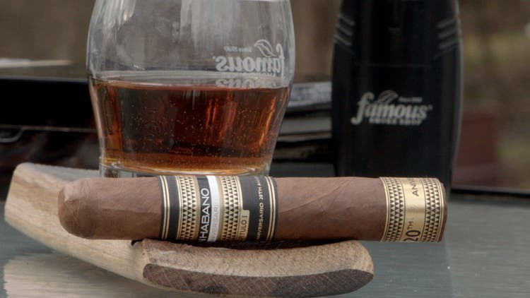 cigar advisor #nowsmoking cigar review gran habano xx aniversario - setup shot of the cigar and whiskey glass on a barrel stave with famous lighter in the background