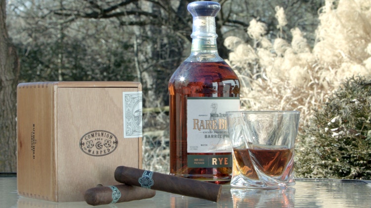 cigar advisor cigar panel review of companion de warped - cigars in front of box with a bottle and glass of spirits in the background