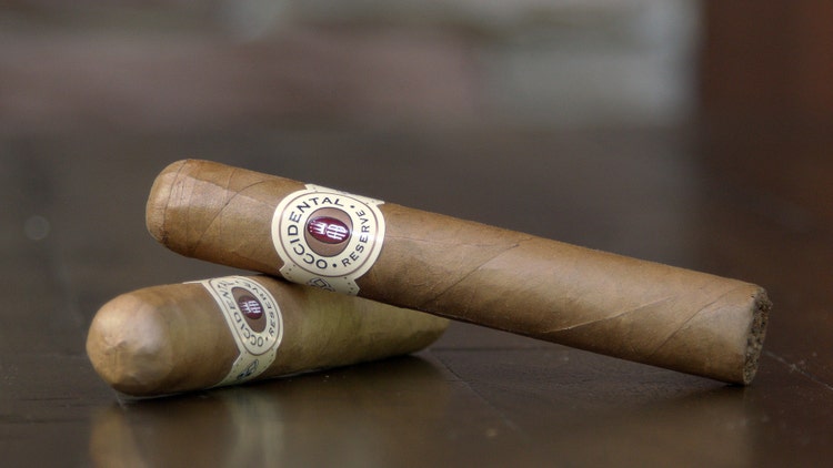 Two Alec Bradley Occidental Reserve Connecticut cigars sitting on a table outside of their cello