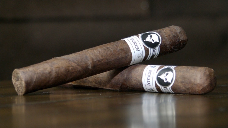 Two J Fuego Vudu Broadleaf cigars are placed on a tabletop for this photo
