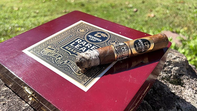 cigar advisor panel review aganorsa leaf rare leaf reserve maduro - setup shot of cigar with ash on top of its box on a bright, sunny day