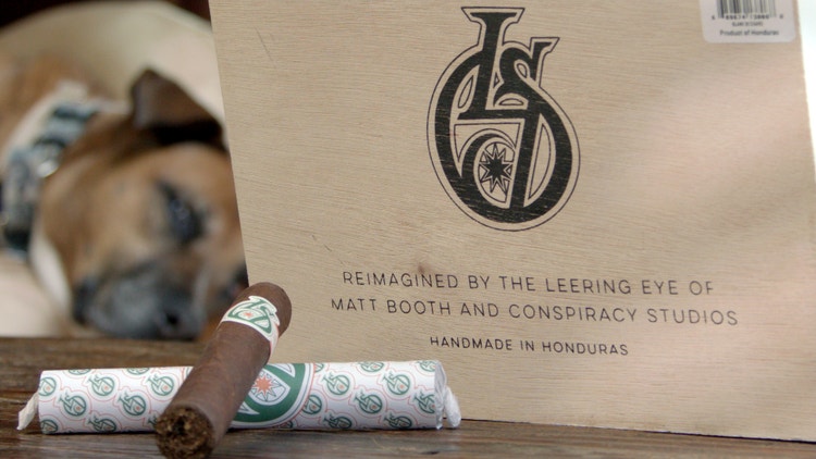 Cigar advisor #nowsmoking cigar review Los Statos Deluxe cigar on table in wrapper with box, dog laying on the couch in the background