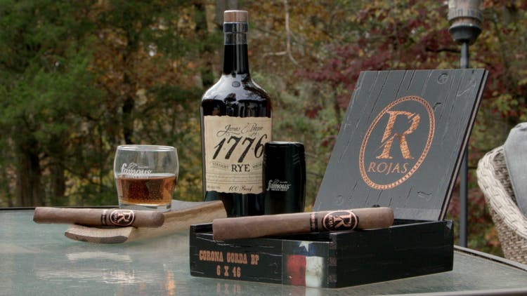 cigar advisor #nowsmoking cigar review of rojas unfinished business - setup shot with cigar, box, and whiskey in the background