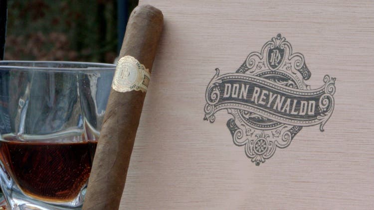 cigar advisor #nowsmoking cigar review don reynaldo regalos by warped - set up shot of cigar leaning against box with whiskey in the background