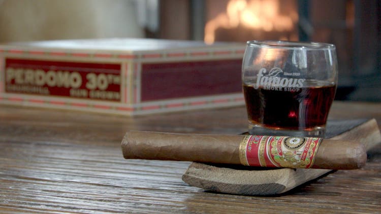 cigar advisor panel review perdomo 30th anniversary sun grown - setup shot of the cigar on a whisky stave with a glass of bourbon and its box and a fireplace in the background