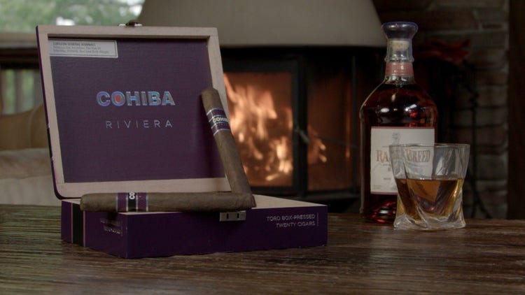 cigar advisor #nowsmoking cigar review cohiba riviera - setup shot of the cigars with whisky and a fireplace in the background