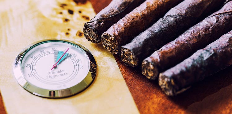 five cigars are near a hygrometer that helps to measure the RH of the humidor they're in